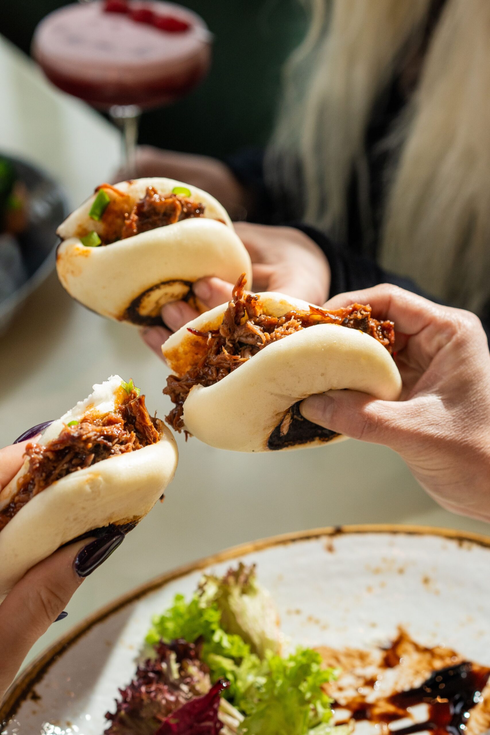 Close-up of hands holding delicious Asian bao buns with shredded meat.