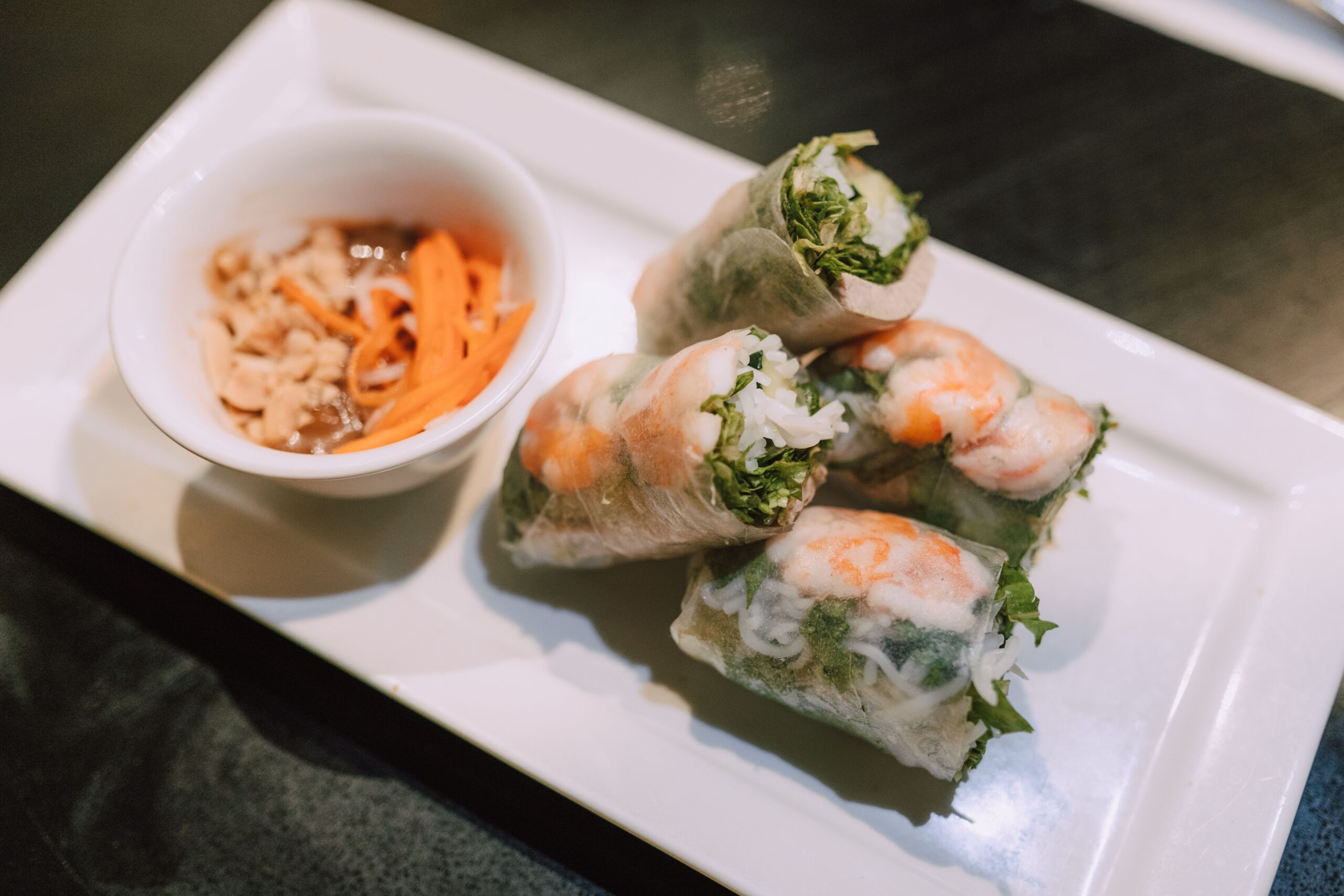 Close-up of Vietnamese spring rolls with shrimp and dipping sauce on a white plate.